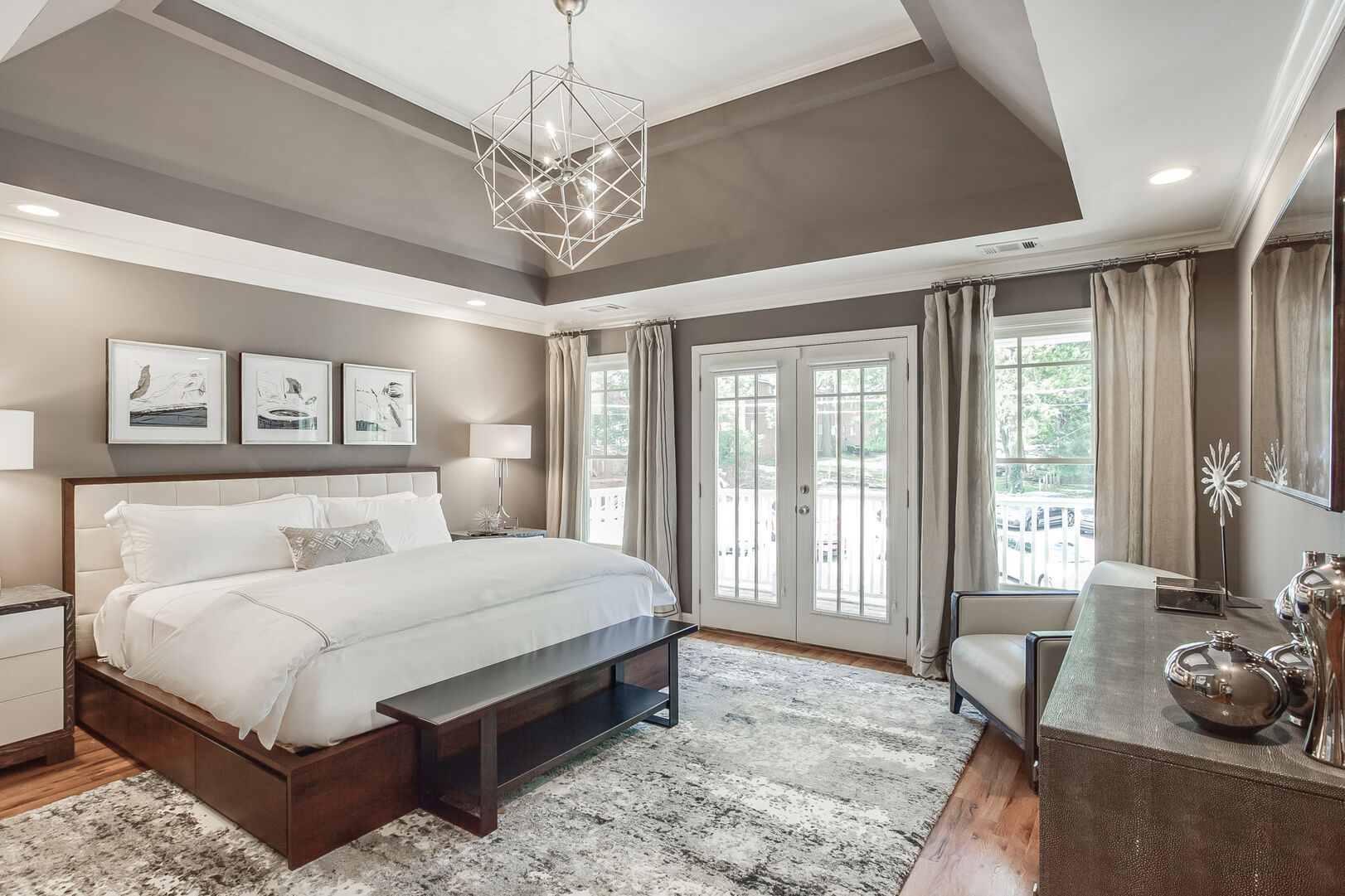 Bedroom with Large Bed, Nightstands, Lamps, Dresser, TV, and Window Doors to the Balcony.