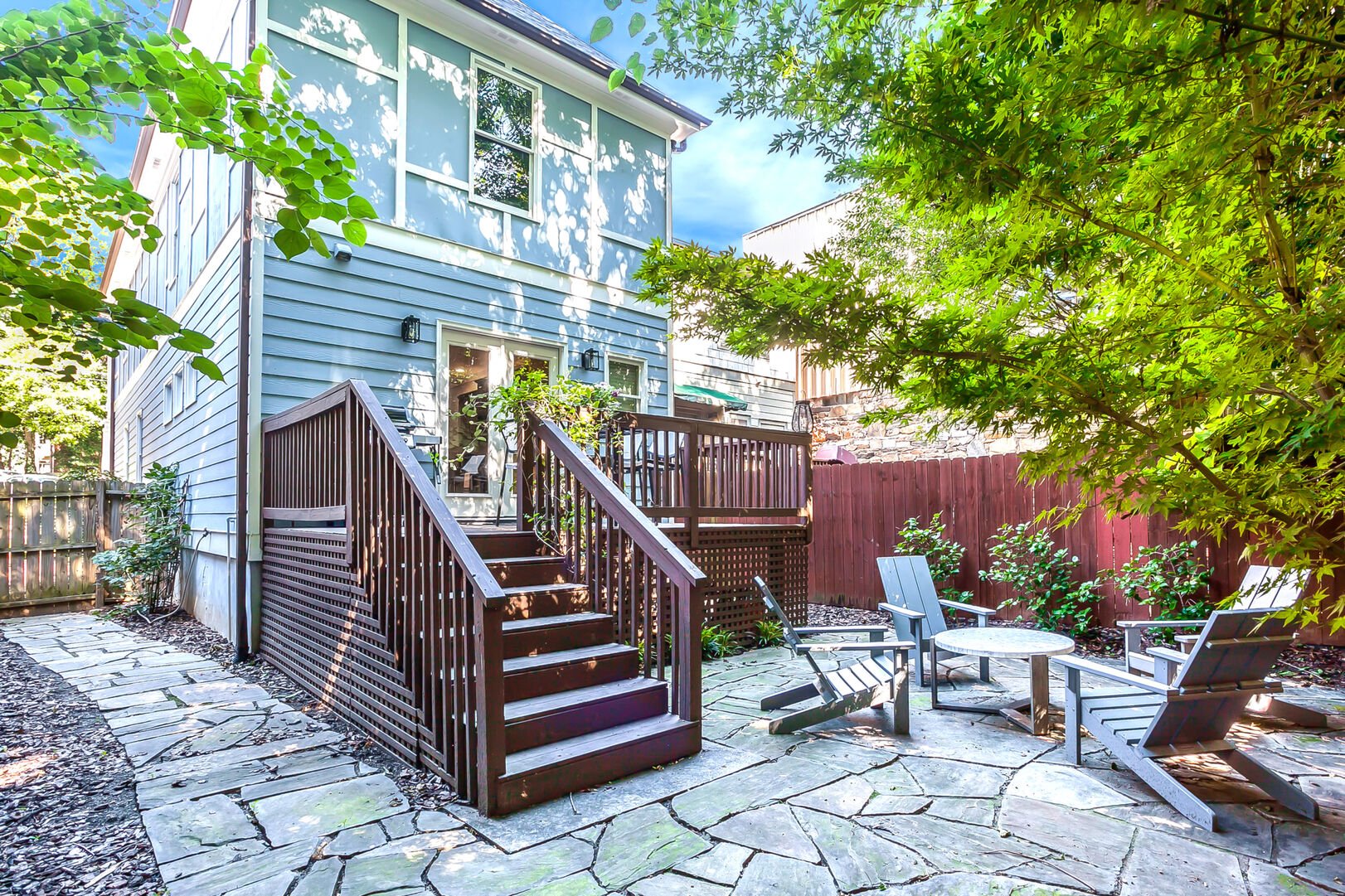 The Backyard with Deck, BBQ Grill, Outdoor Chairs, a Coffee Table, and Trees.